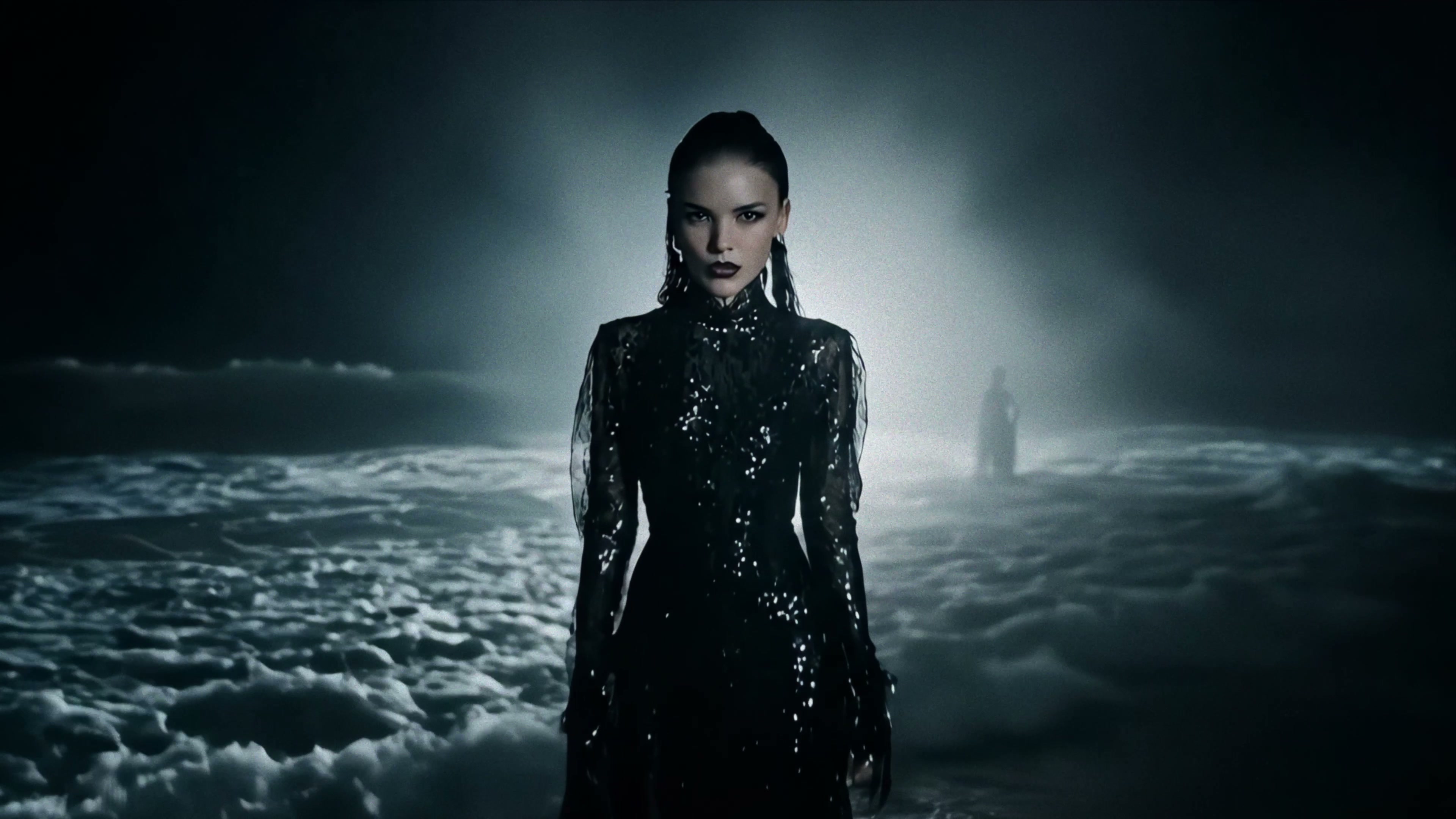 Alexandra Oz. in «Echoes» — a portrait in a wet black sequin dress against a moonlit sea, a lighthouse behind her.