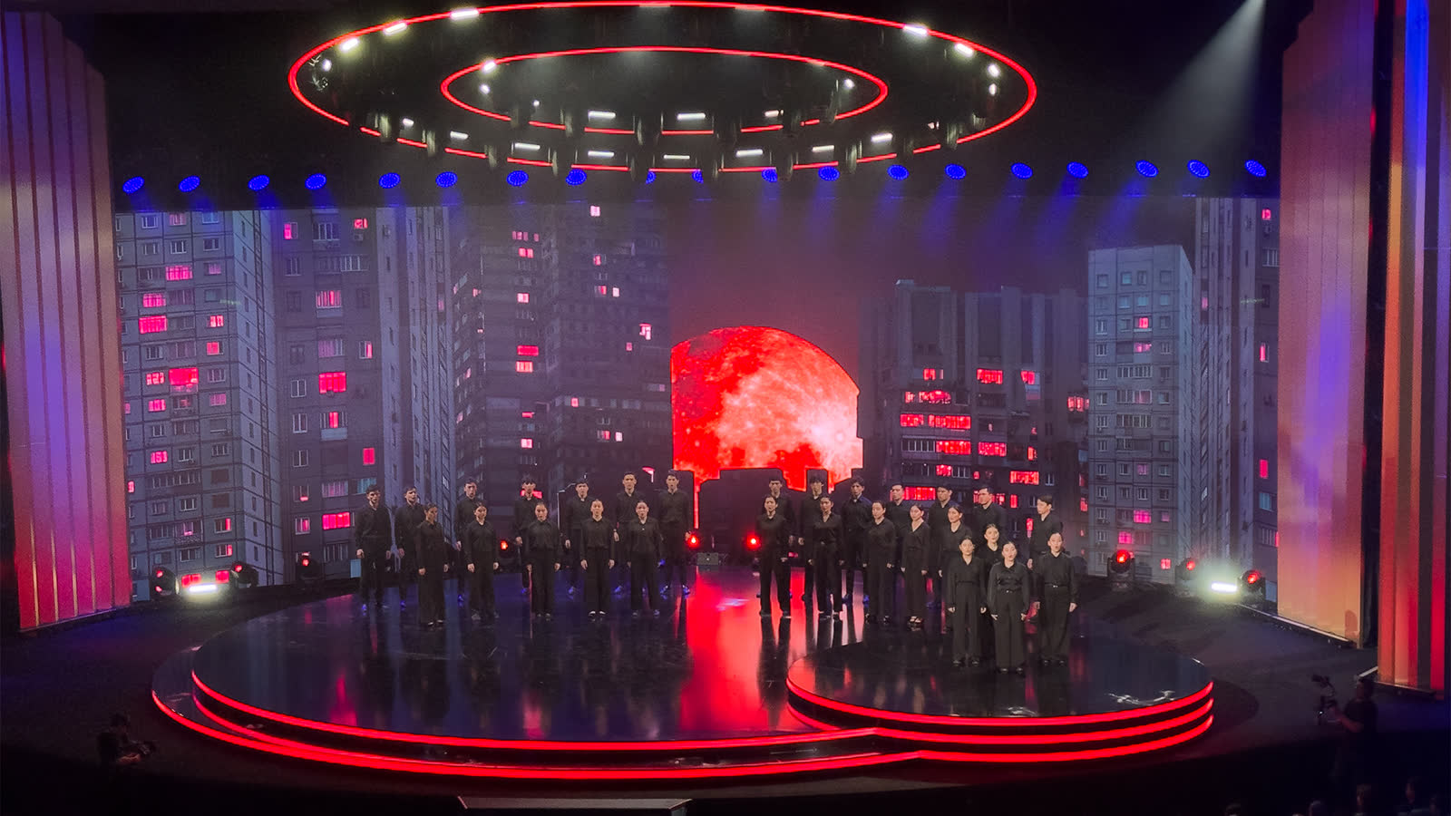 The round stage under its ring truss, the wide screen lit behind the ensemble.