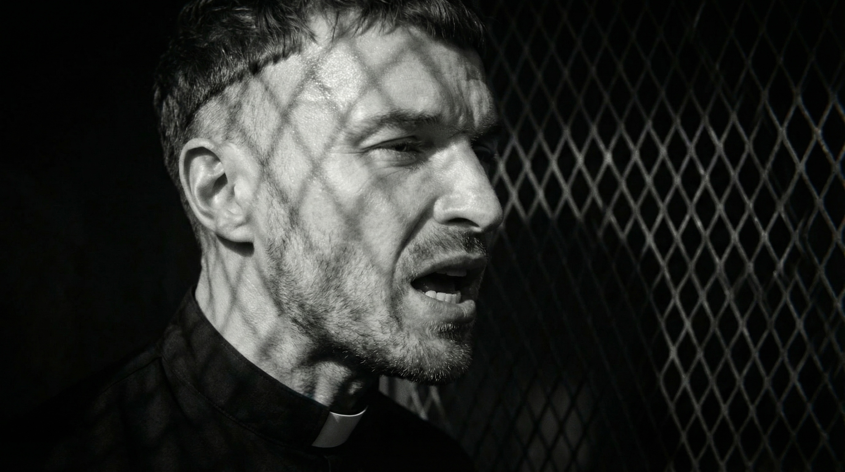 Behind the grille — rhombus shadows raking the priest’s face